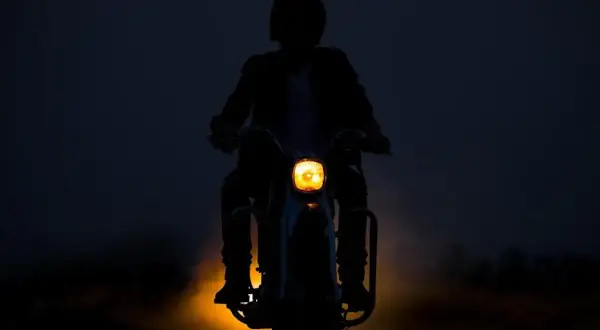 Silhouette d'une personne conduisant une moto dans l'obscurité, le phare jaune illuminant la route. L'aventure de conduire la nuit.