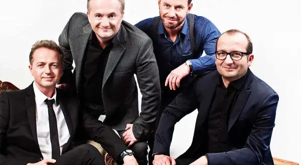 Czterech mężczyzn, członkowie Kabaretu Moralnego Niepokoju, pozuje do zdjęcia w eleganckich garniturach.
