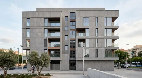 Edificio moderno con revestimiento fachada ventilada de piedra gris, balcones acristalados y detalles en madera. Un ciclista pasa frente a los olivos.
