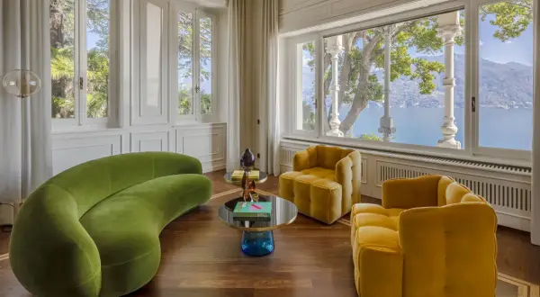 Un salotto con divano verde sinuoso e poltrone gialle, tavolini rotondi e vista lago. Un perfetto esempio di art deco interior design.
