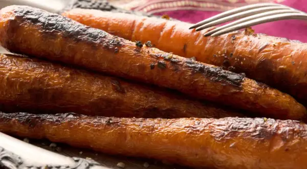 Carottes rôties, caramélisées et légèrement grillées, servies sur une assiette avec une fourchette. Un délice croustillant et savoureux.