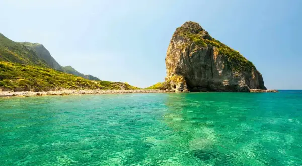 Acque cristalline e un'imponente roccia emergono dal mare bello del Lazio, con colline verdi che si estendono all'orizzonte.
