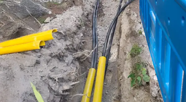 Kabel elektryczny w ziemi, chroniony żółtymi osłonami, przygotowany do zakopania zgodnie z przepisami.