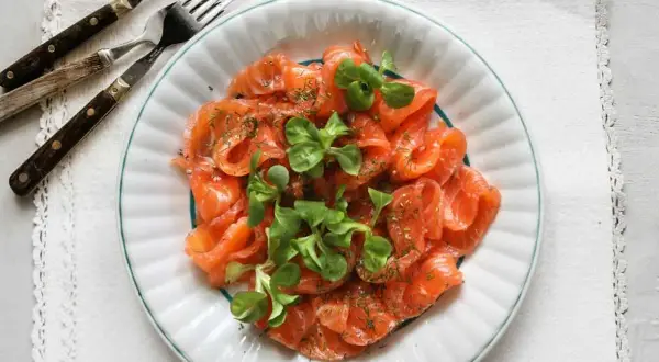 Vacker tallrik med gravad lax, garnerad med dill och gröna blad. Frågan är om man kan frysa gravad lax för att spara den till senare.