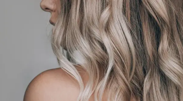 Kobieta z falowanymi, blond włosami w odcieniu sombre. Delikatne przejścia kolorów dodają głębi.