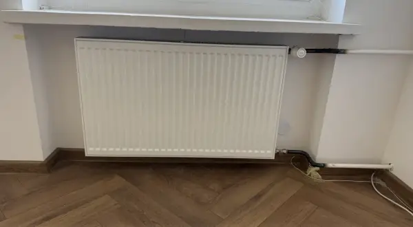 Biały grzejnik pod oknem, nowe podłączenie. Zastanawiasz się, ile kosztuje wymiana kaloryfera?