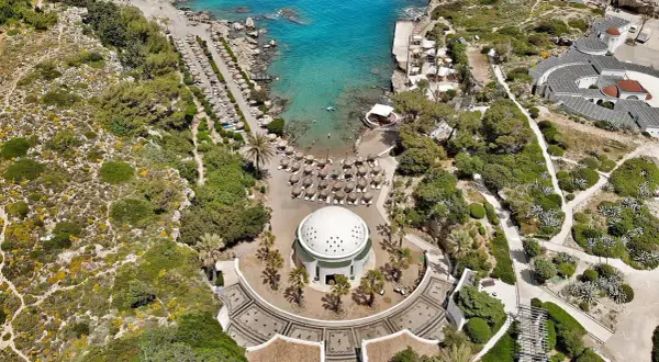 Vacker vy över Kallithea Beach med turkost vatten, solstolar och en kupolformad byggnad.