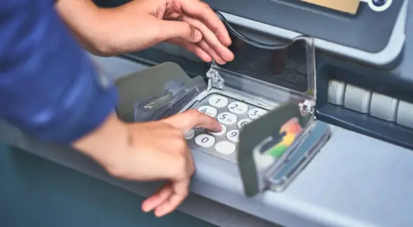 Dłoń wprowadza PIN do bankomatu, pokazując, jak włożyć kartę do bankomatu i dokonać transakcji.
