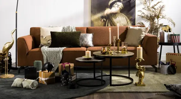 Salon chaleureux avec canapé rouille, coussins texturés et décorations dorées. L'ambiance est réconfortante, avec des touches de **couleur cooper** apportées par des bougies et des statuettes d'éléphants.