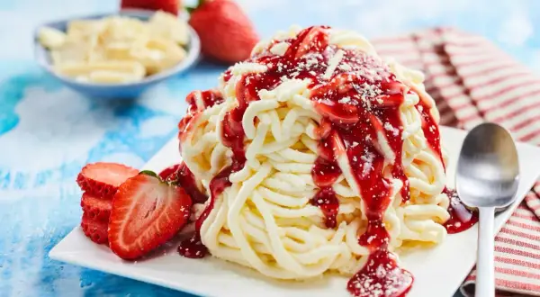 Ein köstliches Spaghetti-Eis mit Erdbeersoße und frischen Erdbeeren, bereit zum Genießen.