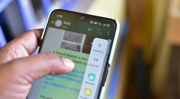 Palec dotyka ekranu telefonu, wybierając opcję "Screenshot", aby pokazać, jak zrobić screena.