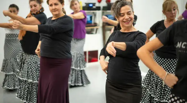 Mujeres aprendiendo como se baila el flamenco, con faldas amplias y movimientos de brazos.