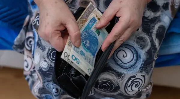 Dłonie wkładają polskie banknoty do portmonetki. Zastanawiasz się, co oznacza zawieszenie renty? To może być trudne, gdy pieniądze są potrzebne.