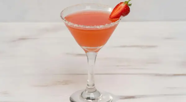 En rosa strawberry daiquiri i ett martiniglas med socker på kanten och en jordgubbsklyfta som garnering.