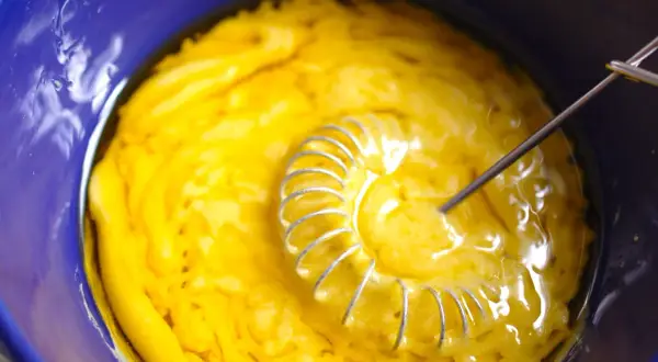 Gelbe Masse wird in blauer Schüssel mit Schneebesen verrührt. Das ist die Basis für eine leckere Vinaigrette.