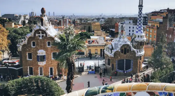 Bunte Mosaike und märchenhafte Gebäude im Park Güell, ein Wahrzeichen von Barcelona. Die Skyline der Stadt im Hintergrund.