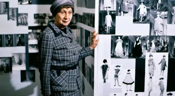 Jadwiga Grabowska, w kratkowanym kostiumie, prezentuje kolekcję zdjęć z pokazów mody.
