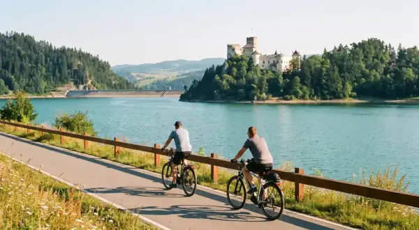 Dwóch rowerzystów na ścieżce Velo Dunajec Czorsztyn, zamek w tle i turkusowa tafla jeziora.