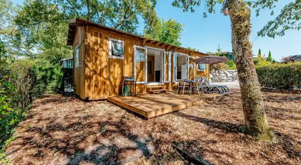 Charmante cabane de pêcheur en bois, avec terrasse, mobilier extérieur et barbecue, nichée dans un cadre verdoyant.