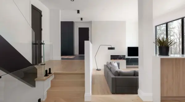 Modern split level home interior with a glass-railed staircase, a gray sectional sofa, and a fireplace.