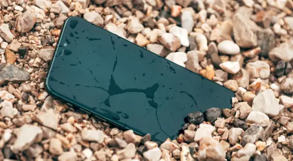 Smartfon leży na kamieniach, mokry, ale wytrzymały zgodnie ze **standardem militarnym MIL-STD-810H**.