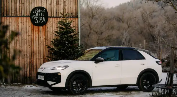 Biały, mały SUV zaparkowany obok drewnianej chaty z napisem "Polna Hill SPA" i choinką ozdobioną lampkami.