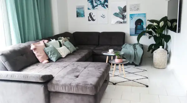 Gemütliches wohnzimmer einrichten mit einer großen, dunklen Couch, vielen Kissen in Pastelltönen und mintgrünen Akzenten. Bilder und eine Pflanze schmücken die Wand.