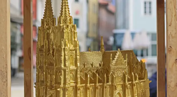 Goldene Nachbildung des Regensburger Doms mit filigranen Figuren und Türmen, die vor einer unscharfen Stadtkulisse steht.