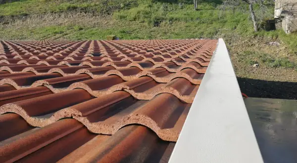 Tegole per tetti a bassa pendenza, color terracotta, disposte in file ordinate su un tetto. Sullo sfondo, un pendio erboso.