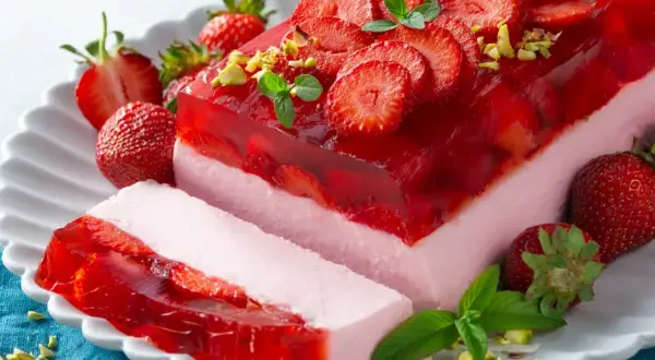 Pyszny sernik na zimno z galaretką i truskawkami, udekorowany miętą i pistacjami. Idealny na letnie popołudnie.
