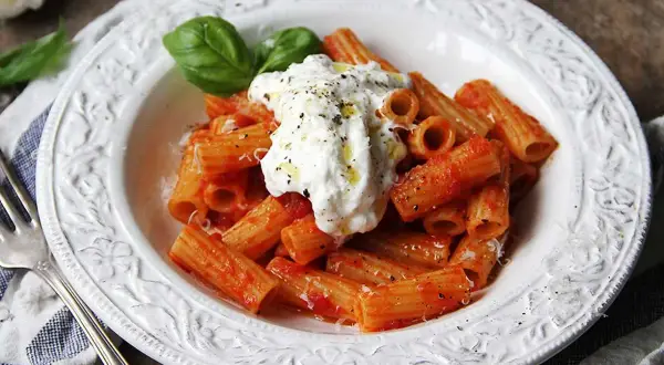 En krämig burrata pasta med rigatoni i tomatsås, toppad med färsk basilika och svartpeppar.