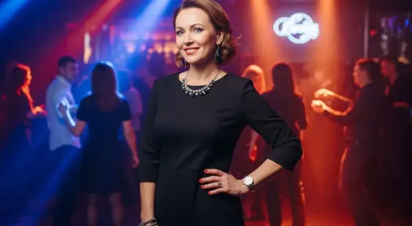 Elegancka kobieta w czarnej sukience, idealna inspiracja, jak się ubrać na dyskotekę po 40. Taniec w blasku świateł.