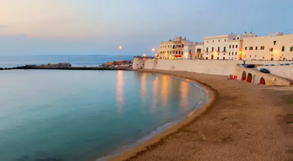 La costa di un paese vicino a Lecce al tramonto, con edifici bianchi, una spiaggia sabbiosa e il mare calmo.