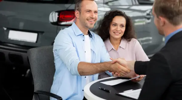 Un couple heureux finalise un accord de rachat de franchise avec un concessionnaire automobile, scellant leur nouvelle acquisition par une poignée de main.