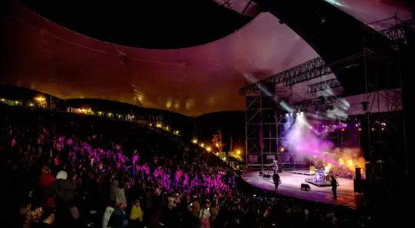 Koncert na amfiteatrze w Mrągowie, oświetlona scena i publiczność.