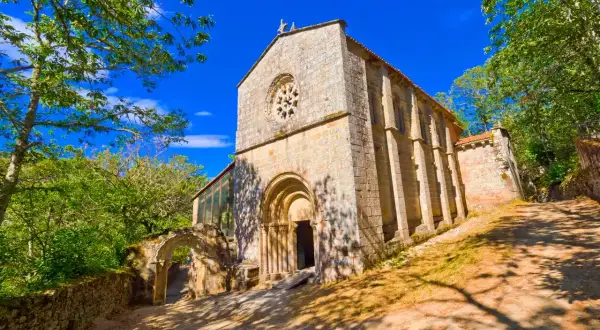 Monasterio de Santa Cristina de Ribas de Sil, una joya románica rodeada de exuberante vegetación bajo un cielo azul intenso.