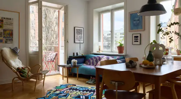 En ljus och färgstark lägenhet med 60-tals inredning. En blå soffa med mönstrat överkast, en trästol med fårskinn och en lekfull matta på parkettgolvet.