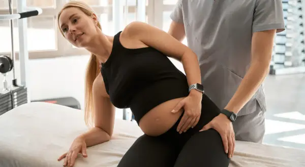 Fisioterapeuta ayuda a una embarazada con dolor de cadera al dormir.