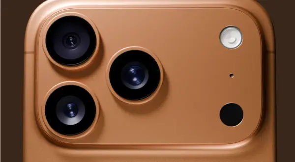 Gros plan sur le module caméra d'un iPhone couleur or. Trois objectifs noirs et un flash blanc sur un fond brun.