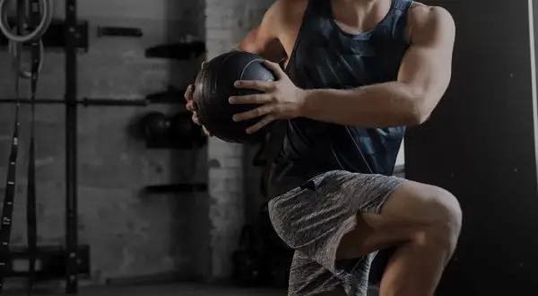 Uomo in palestra esegue un esercizio con palla medica. Gli aminoacidi essenziali a cosa servono? Aiutano la costruzione muscolare.