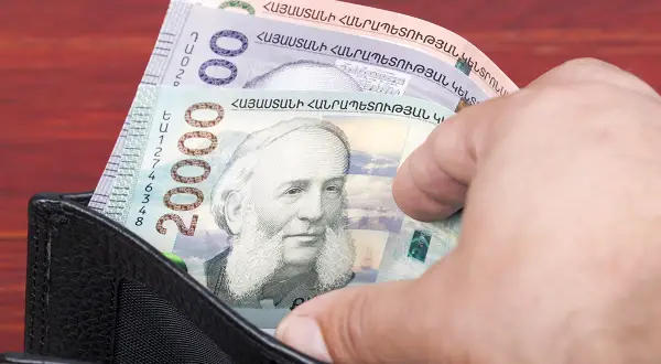 Dłoń wyciąga z portfela banknot 20000 dramów, waluta Armenii. Widoczne też inne banknoty.