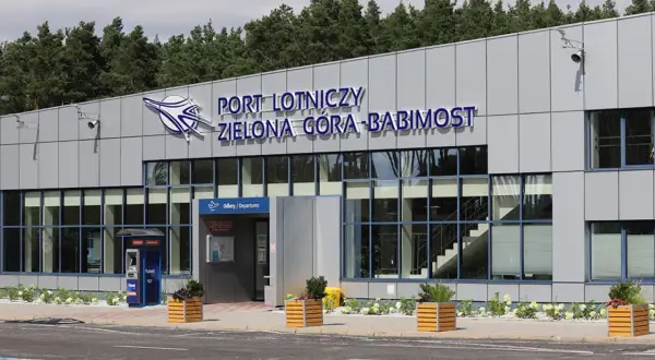 Nowoczesny budynek lotniska w Zielonej Górze-Babimoście z dużymi oknami i napisem "PORT LOTNICZY ZIELONA GÓRA-BABIMOST".