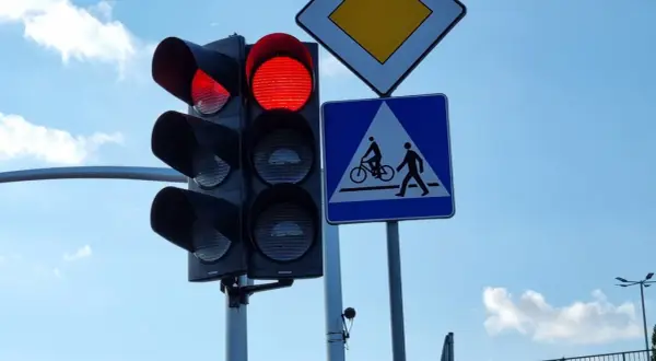Czerwone światło na sygnalizatorze drogowym, obok znak d6 informujący o przejściu dla pieszych i rowerzystów.