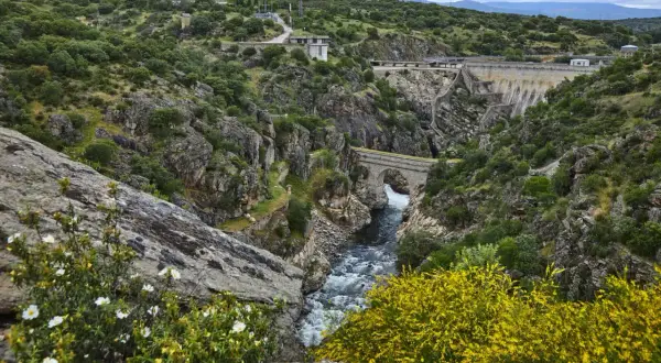 Paisaje natural con un río caudaloso, un puente de piedra y una presa. Un lugar ideal que ver en Robledillo de la Jara para disfrutar de la naturaleza.