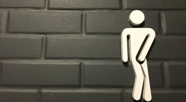 Biały symbol mężczyzny na ciemnej, ceglanej ścianie. Może symbolizować problemy z oddawaniem moczu, takie jak niskie ciśnienie moczu u mężczyzn.