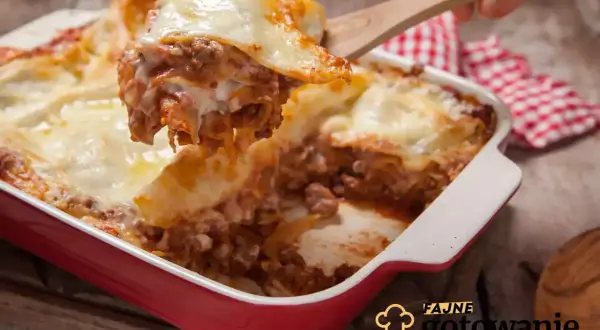 Gorąca, pachnąca lasagne z mięsem i serem, właśnie nakładana drewnianą łopatką. Idealna na rodzinny obiad.