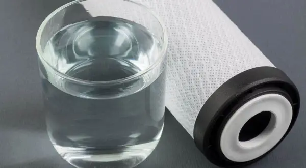 Un bicchiere d'acqua limpida accanto a un filtro. Per mantenere l'acqua pura, è importante sapere ogni quanto cambiare sali caldaia.
