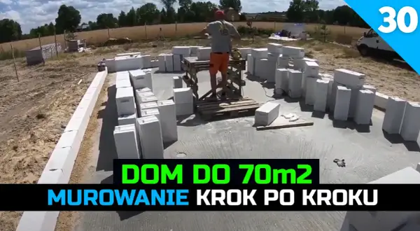 Budowa domu 70m2: murowanie ścian z bloczków betonowych. W tle plac budowy i pracownik.