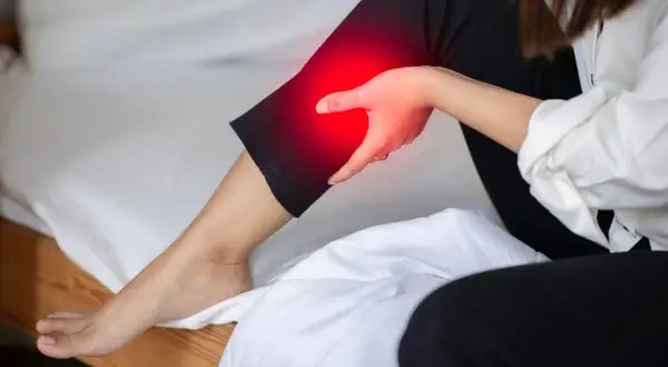 A person holds their leg, which is highlighted in red, indicating pain. This image explores the question: can a bad mattress cause leg pain?
