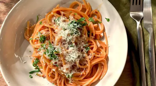 En tallrik med god pasta, toppad med riven ost och färska örter. En gaffel och kniv ligger bredvid.